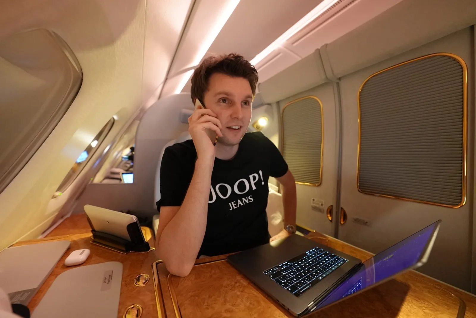 Frank arbeitet mit Laptop und Telefon in der First Class eines Flugzeugs
